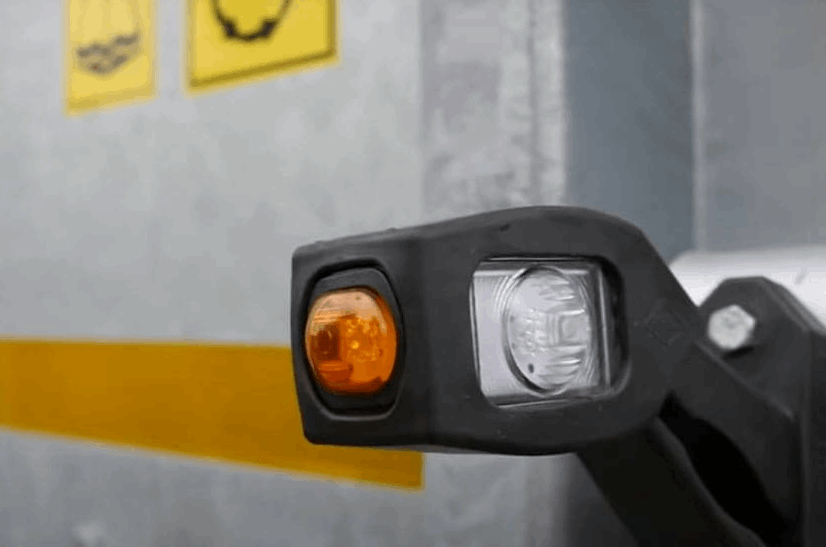 Close-up of a trailer marker light assembly with warning labels in the background