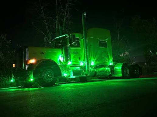 A commercial truck displayed at night with green auxiliary lights illuminated while parked on private property.