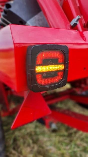 Close-up of RoadLites ROCA LZD 2800 LED Rear Lamp with brake, position & indicator lights mounted on farming or agricultural machinery outdoors and illuminating amber and red lights.