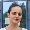 Portrait of a young woman with dark hair wearing a light-colored top standing outdoors near a glass building
